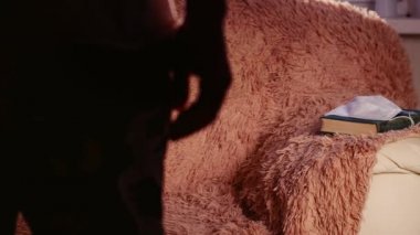 Bir adam bir kanepeye oturur ve elinde bir kitap tutar. Kitapta tıbbi bir maske var.