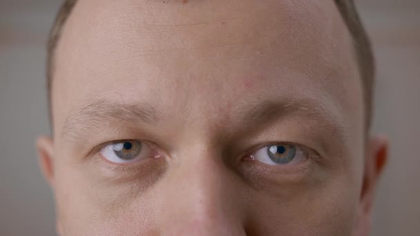 Egy szürke szemű fiatalember arca, aki egyenesen a kamerába néz, közelről. — Stock videók