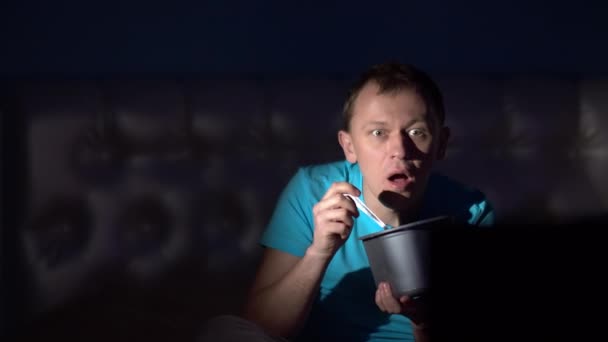 Ένας άντρας βλέπει τηλεόραση τη νύχτα και τρώει παγωτό. Έκπληκτη φάτσα — Αρχείο Βίντεο
