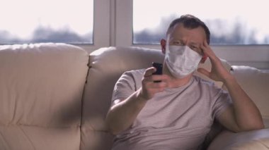 Tıbbi maske takan bir adam evde kanepede oturur ve televizyon seyreder, kamerayı oynatır. Kişisel izolasyon kavramı