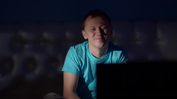 Attractive man in a blue T-shirt watching television in the late evening laughing — Stock Video