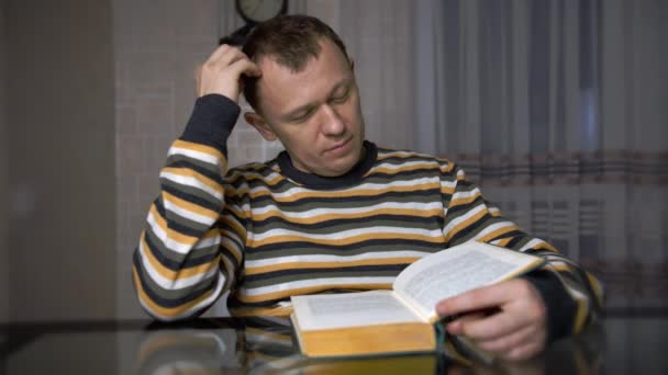 Un jeune homme étudie un texte dans un livre vert assis à une table . — Video