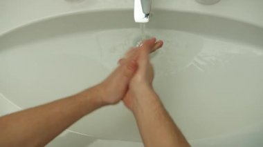 Bir adam ellerini musluğun altında sabunla yıkıyor.