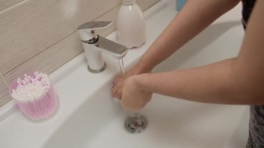 Kız ellerini musluğun altında suyla yıkıyor.
