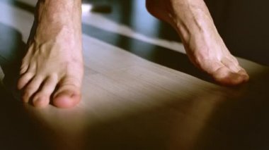 Aydınlık bir zeminde yalın ayak zıplayan bir adamın bacakları