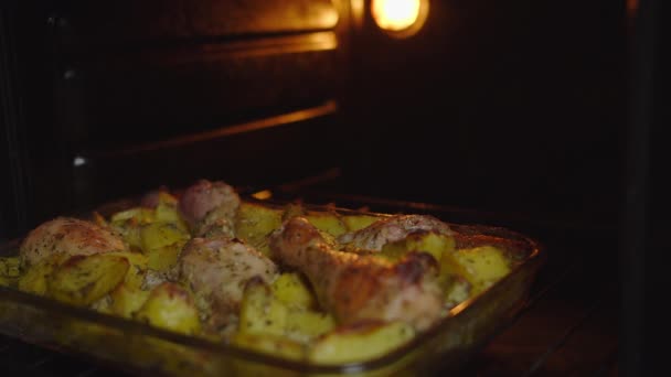 男は焼きたての鶏の足とジャガイモとオーブンからベーキングシートを取り出します — ストック動画