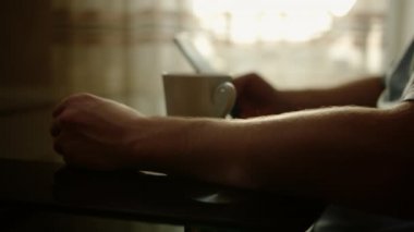 Adam masaya oturur, kahve içer ve cep telefonu kullanır, yakın plan, odaklanma vardiyası.