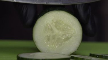 Siyah eldivenli bir aşçı taze bir salatalık dilimliyor.