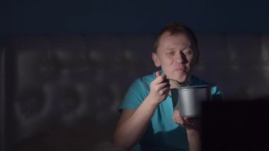 Bir adam akşam televizyon izlerken gülüyor ve dondurma yiyor.