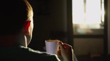 Bir kupa sıcak içeceği olan bir adamın silueti, gündoğumunun arka planı, dikiz açısı, kamera hareketi