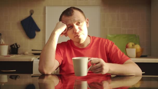 一个男人坐在厨房的桌子旁，喝着阳光灿烂的巢穴宠物茶，看着相机的画像 — 图库视频影像