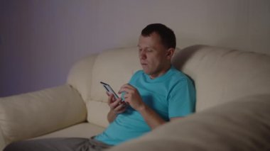 Genç bir adam akşamları kanepede oturup telefondaki mesajlara bakar.