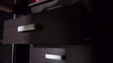 Siyah eldivenli hırsız elbiseli çekmecelerde para arıyor.