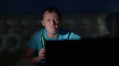 Öfkeli adam elinde birayla oturur televizyon seyreder, olumsuz duygular, kamera hareketleri.