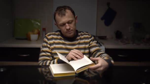 男は夜遅くテーブルに座り本を読む — ストック動画