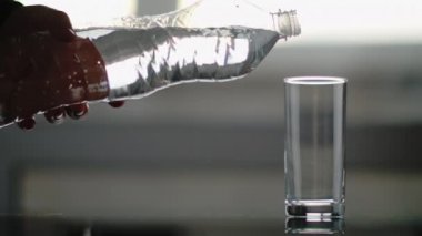 Plastik şişeli bir erkek eli cam bardağa temiz su döker.