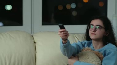 Gözlüklü hoş kız akşamları kanepede oturur ve televizyon izler.