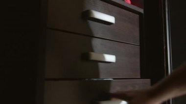 Gecenin geç saatlerinde, bir adam çamaşır çekmecesinde bir şey arıyor, kamera hareketi.
