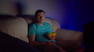 Bir adam gece geç saatlere kadar kanepede oturup patates cipsi yerken ilginç bir program izler.