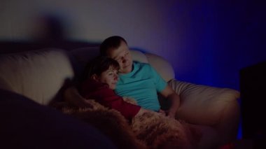 Evli çift gece geç saatlere kadar kucaklaşır ve kanepede otururken televizyon izlerler.