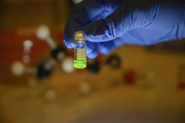 Scientist holding a greeen colour solution in a glass vial weari