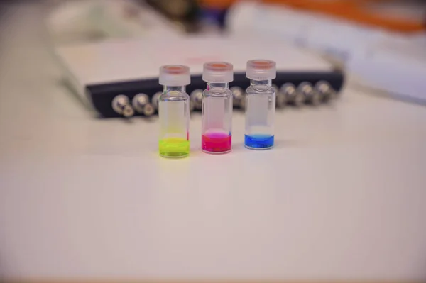 Três soluções coloridas em diferentes frascos para injetáveis de vidro LCMS sobre um branco — Fotografia de Stock