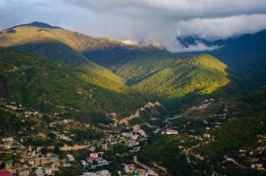 Buda noktasından Thimphu şehrinin panoramik görüntüsü dağların tepelerini kaplayan bulutları ve bazı tepelerden gelen güneş ışığını gösteriyor.