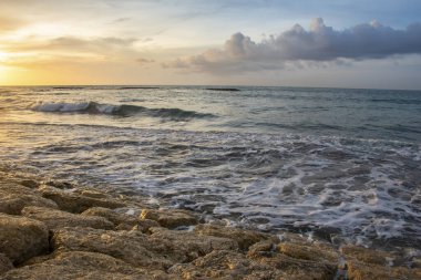 Endonezya, Bali 'de yaz mevsiminde deniz kenarındaki bulutların üzerinde gün batımından doğan güneş ışığı
