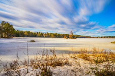 İsveç 'in kuzeyindeki çam ağaçlarıyla çevrili donmuş bir göl üzerinde hareketli güneş bulutunun çarpıcı renkli görüntüsü