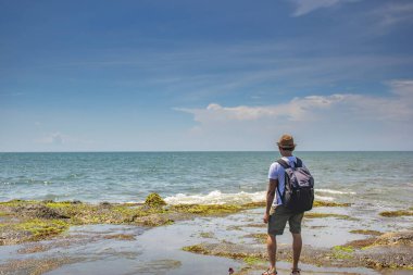 Gökyüzünde bulut ve taş yüzeyine vuran yeşil suyla dolu güzel bir deniz manzarası Endonezya, Bali 'deki bir turist tarafından keyifle izleniyor.