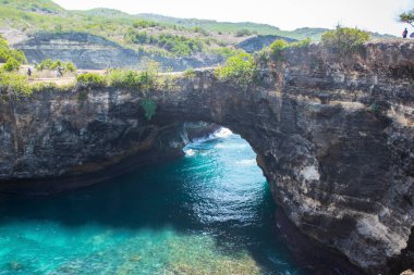 Nusa Penida, Bali 'deki turistik ziyaret sırasında tepeden gelen kırık sahil kıyısı yeşil-su dalgası manzarası