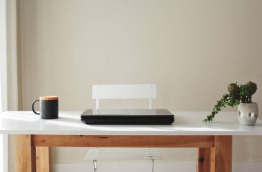 Kahve fincanı bilgisayarı ve bitkisi olan ahşap masa.