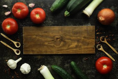 Etrafı sebzelerle çevrili ahşap kesme tahtası ve biberli ahşap kaşıklar ve karanfil.