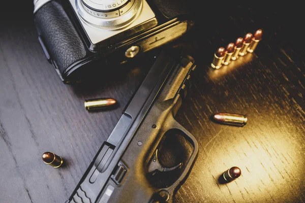 Pistol, camera and bullets on wooden table