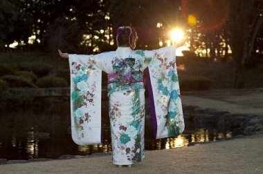 Japanese teenager wearing traditional kimono back and arms outstretched with beautiful flare and sunshine celebrating the Coming of Age Day in Fuji City, Japan. Horizontal shot. clipart