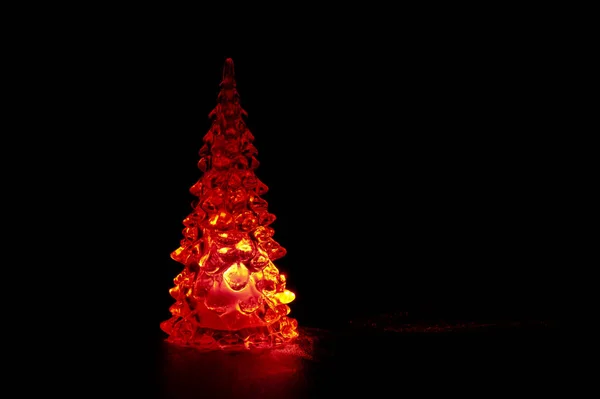 Glass Christmas tree with red led isolated on black background. Copy space on the right. Horizontal shot.