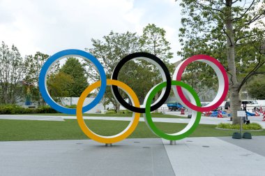 SHINJUKU CITY, TOKYO, JAPAN - SEPTEMBER 30, 2019: Front view of Olympic Rings. Background with New National Stadium (Tokyo) and the Cauldron (The XVIII Olympic Games Nagano 1998). Horizontal shot. clipart