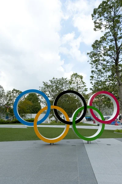 Shinjuku Şehri, Tokyo, Japonya - 30 Eylül 2019: Olimpiyat Halkaları 'nın ön görüntüsü. Yeni Ulusal Stadyum (Tokyo) ve Kazan (The Xviii Olympic Games Nagano 1998) ile arka plan. Dikey çekim.