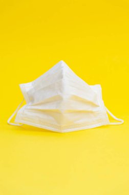 Coronavirus (COVID-19) ve diğer bulaşıcı hastalıklara karşı korunmak için beyaz cerrahi maske. Sarı arka planda izole edilmiş. Yakın plan. Uzayı kopyala Dikey çekim. 