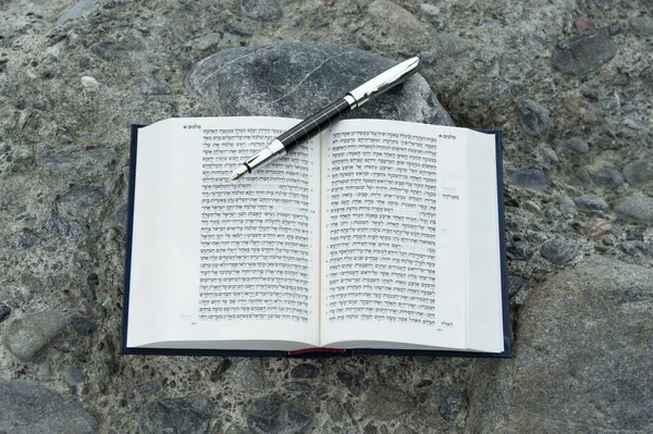 Open Hebrew Bible - TANAKH (Torah, Neviim, Ketuvim - The Law, The Prophets, The Writings) with fountain pen outdoors. Isolated on stones background. Horizontal shot. Close-up.