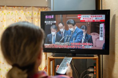 Fuji Şehri, Shizuoka, Japonya - 7 Nisan 2020: Bir kadın Japonya Başbakanı Shinzo Abe 'i televizyonda, koronavirüs salgınının yayılmasını kontrol altına almak için olağanüstü hal ilan edilmesi hakkında izliyor (COVID-19).