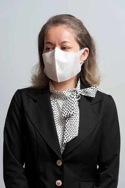 Half body portrait of middle-aged mixed race woman in formal wear wearing white disposable 3D face mask for protection against novel Coronavirus (SARS-CoV-2) and COVID-19. Isolated on white background. Looking to the side.