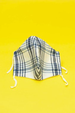 Koronavirüse karşı korunmak için mavi ve beyaz (DIY) ev yapımı yüz maskeleri (COVID-19). Sarı arka planda izole edilmiş. Uzayı kopyala Dikey çekim.