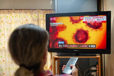 Fuji Şehri, Shizuoka, Japonya - 7 Nisan 2020: Bir kadın Japon televizyonunda koronavirüsün yayılması (COVID-19) ile ilgili bir haber yayını izliyor.