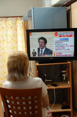 Fuji Şehri, Shizuoka, Japonya - 14 Mayıs 2020: Coronavirus (COVID-19) salgını. Bir kadın Japon televizyonunda Başbakan Shinzo Abe 'in 39 vilayetteki 
