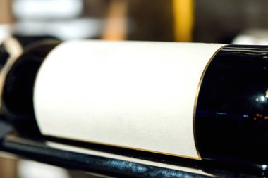 Boş etiketli bir şişe şarap, yakın plan. Bir şişe şarap, yatay pozisyonda duruyor. Etiket beyaz. Metnin altına yerleştir