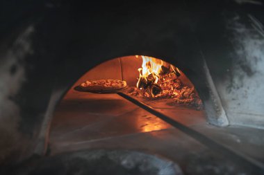 Fırında pizza, yanan odunun yanındaki kürekte.