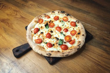 Tahta bir masada peynirli, soslu ve sebzeli taze pişmiş pizza.