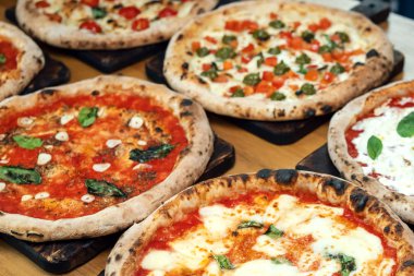 Bir İtalyan restoranında ahşap bir masada bir sürü yeni hazırlanmış pizza.