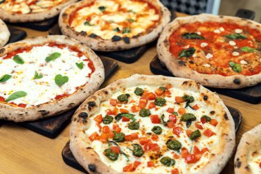 Bir İtalyan restoranında ahşap bir masada bir sürü yeni hazırlanmış pizza.